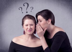 A woman whispering into another woman’s ear, raising doubts.