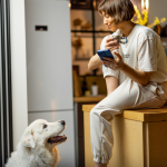 woman smiles at dog while holding her phone and a coffee mug