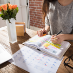 Calm female freelancer is planning her week at a desk with sunlight and fresh flowers