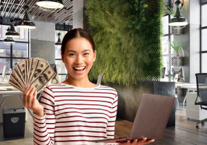 Smiling winning writer holds cash in one hand and her laptop in the other